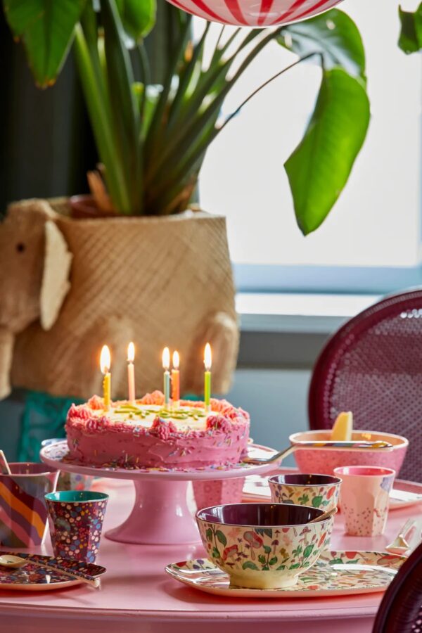 Kuchen- und Tortenplatte von Rice in märchenhaftem Rose mit roten Herzen mit Geburtstagskuchen, auf dem Kerzen brennen Fotografiert.