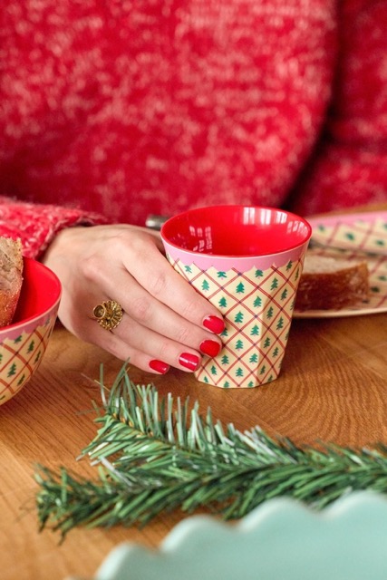 Medium Becher von Rice in Beige mit Allover grünen Tannenbäumen, Rosa Rand und roter Innenfarbe gehalten von Frau mit rotem Pulli und rot lackierten Nägeln