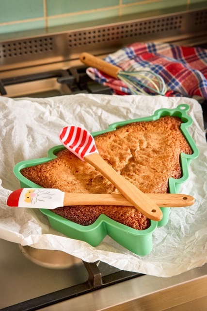 Silikonbackform Weihnachtsbaum in grün von Rice mit einem Kuchen drin und 2 Weihnachts-Silikonschabern darauf liegend