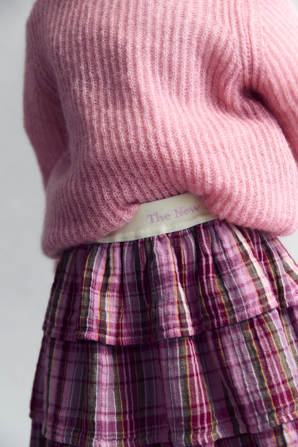 Rosa karierter Baumwollrock mit beige Gummiband in das der Text "The New Society" eingewebt ist.